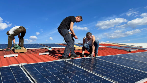 Drie mensen leggen zonnepanelen aan op een dak